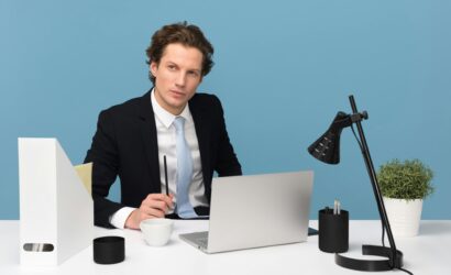 A focused businessman in a suit works at his tidy desk with a laptop, plant, and lamp.