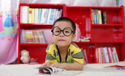 A cute child in glasses reading a book, surrounded by colorful shelves. Perfect shot of childhood learning indoors.