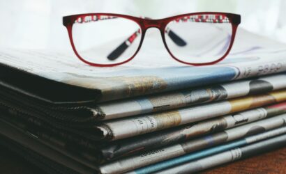 Red eyeglasses resting on a stack of newspapers symbolize reading and information.