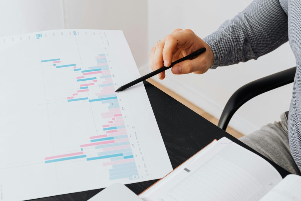 pexels-photo-5717701-5717701 Close-up of a person analyzing a colorful graph chart with a pen in a modern office setting.