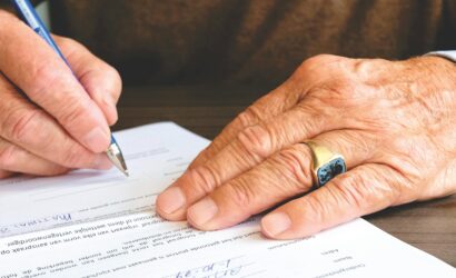 Close-up of a senior adult signing a legal document with a focus on hand and gold ring.