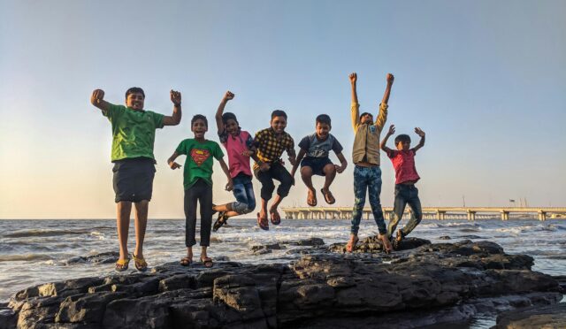 Group of kids joyfully jumping on rocks by the seaside. Fun and playful moment captured outdoors.