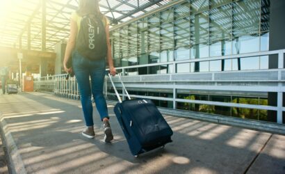 A woman walks with a suitcase outside an airport terminal, ready for travel.
