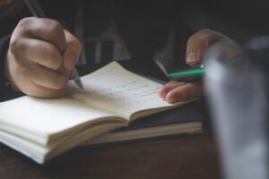 Detail shot of adult hands writing in a notebook, possibly researching or studying.
