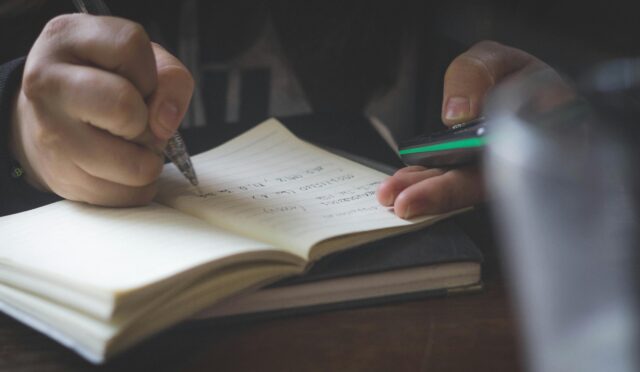 Detail shot of adult hands writing in a notebook, possibly researching or studying.