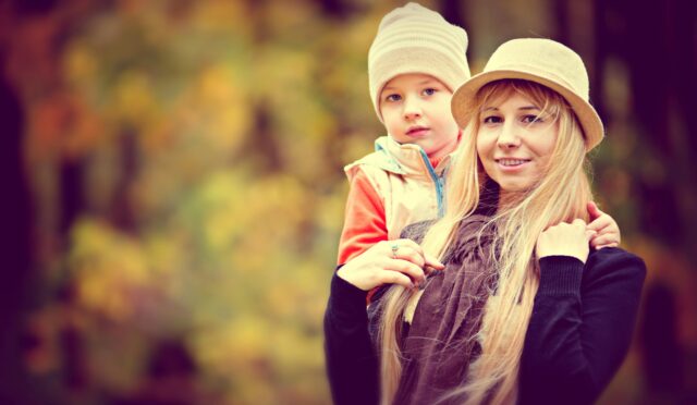 A joyful mother and child in warm hats, enjoying a sunny autumn day outdoors.