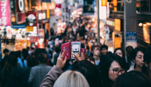 Vibrant street scene in a busy city market with diverse crowds and bright neon signage.