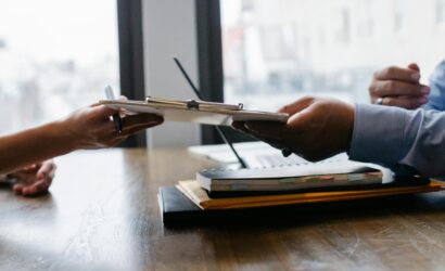 Crop anonymous ethnic woman passing clipboard to office worker with laptop during job interview