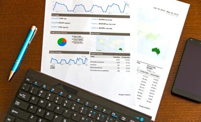 Flatlay of a business analytics report, keyboard, pen, and smartphone on a wooden desk.