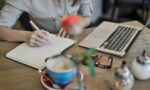 Woman writing in a notebook with a laptop and coffee cup on a desk. Ideal for workspace inspiration.