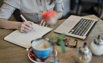 Woman writing in a notebook with a laptop and coffee cup on a desk. Ideal for workspace inspiration.