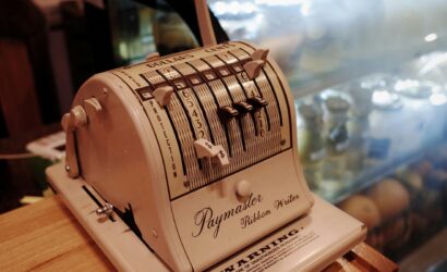 Close-up of a vintage Paymaster Ribbon Writer on a wooden counter in a retro cafe setting.