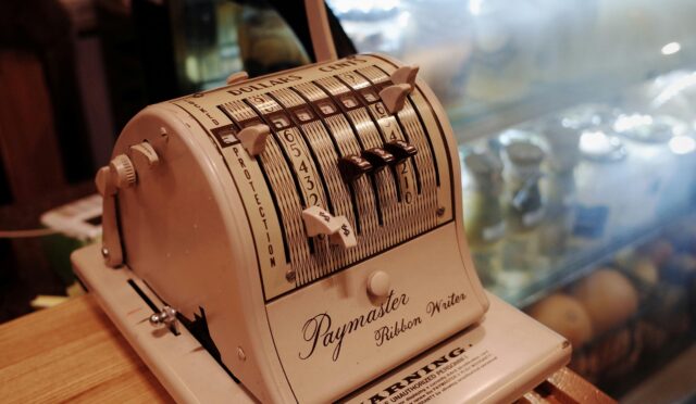 Close-up of a vintage Paymaster Ribbon Writer on a wooden counter in a retro cafe setting.