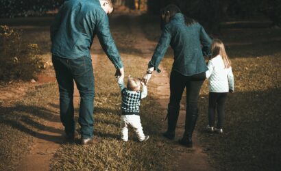A family of four walks hand in hand on a path, enjoying a sunny day outdoors.