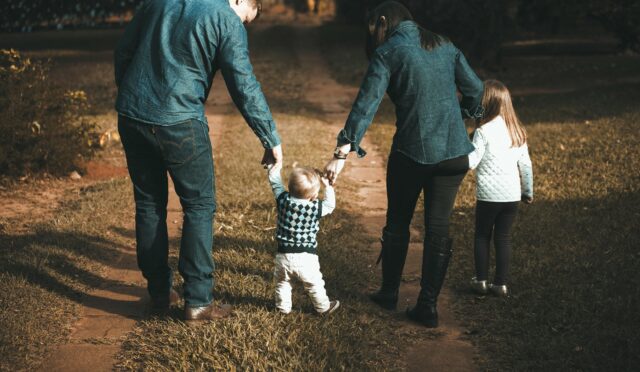 A family of four walks hand in hand on a path, enjoying a sunny day outdoors.