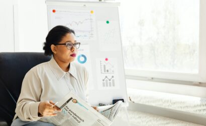 Confident businesswoman reading newspaper and analyzing market trends in a modern office setting.